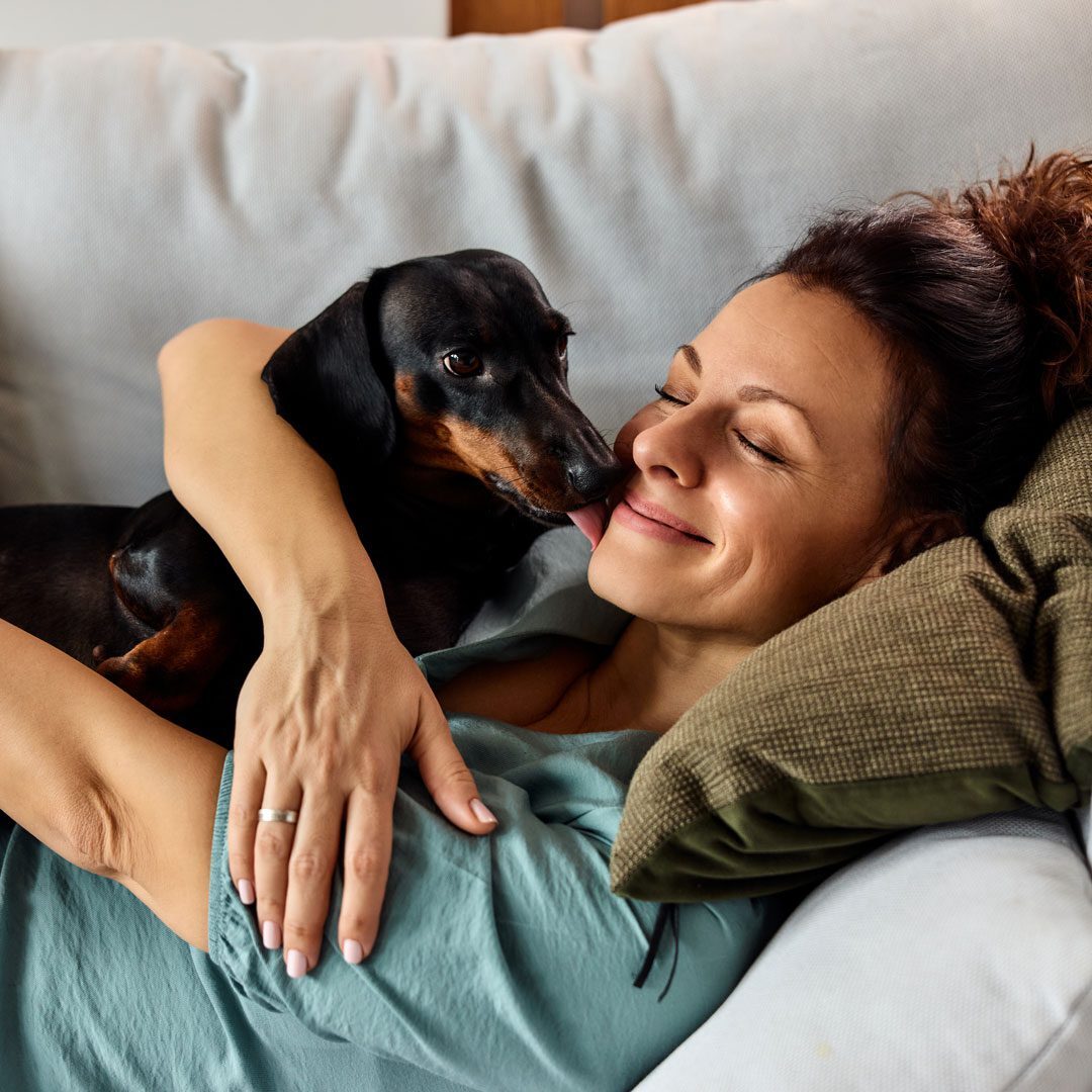 smiling woman laying on the couch holding her dachshund